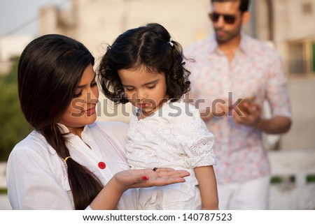 portrait of mother and daughter with father in the background, mother holding her daughter in the lap with father in the background