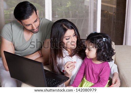 Indian family of three using laptop, young couple relaxing at home