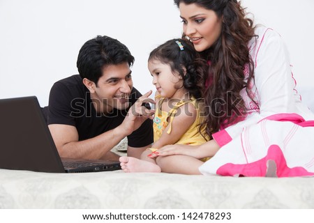 father and mother using laptop with the daughter on bed