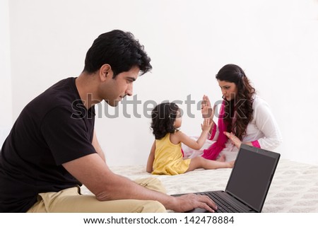 father using laptop while mother and daughter playing in the background