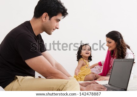 father using laptop while mother and daughter playing in the background