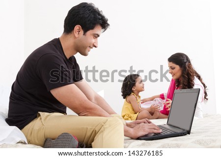 father using the laptop with mother and daughter playing in the background