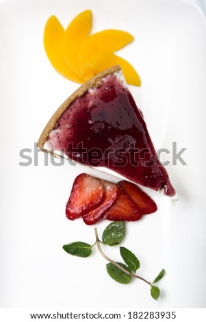 close up of cheese cake with cherry syrup and garnishing of strawberry slices and mint leaves.