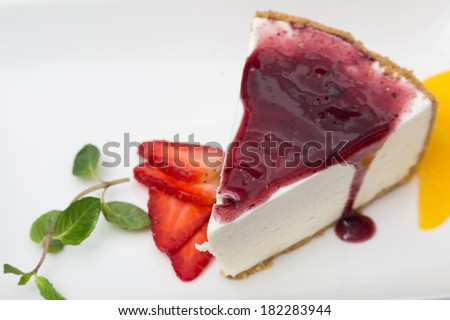 close up of cheese cake with cherry syrup and garnishing of strawberry slices and mint leaves.