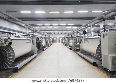 A row of textile looms weaving cotton yarn in a textile mill.