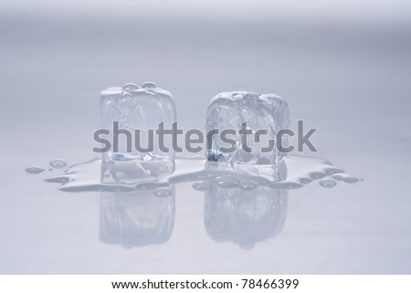 two melting ice cubes and water spill shot on reflective surface