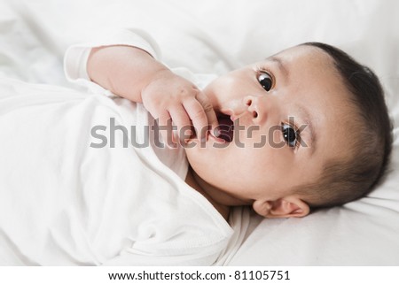 Adorable little baby girl after waking up in the bed. little baby thinking about something, wearing white shirt and laying in the bed with white bed sheet.
