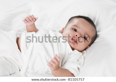 Adorable little baby girl after waking up in the bed. little baby thinking about something, wearing white shirt and laying in the bed with white bed sheet.