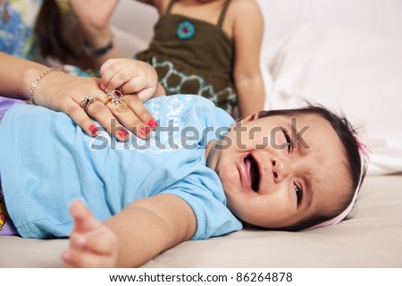 Angry little baby is crying while her mother caresses her with love to calm her down.
