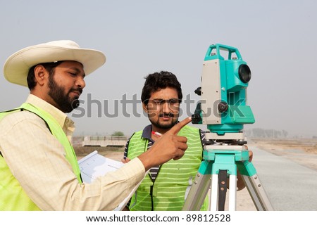 two civil engineers doing a survey on a construction site. Engineers doing land survey at a construction site