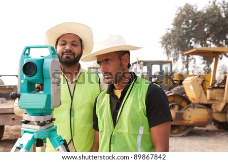 two civil engineers doing land survey at a construction site with construction machinery in the background