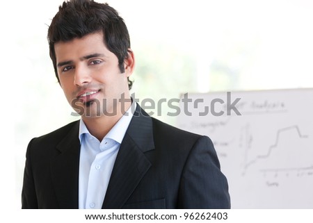 portrait of a happy Indian businessman standing in the boardroom with his colleague in the background