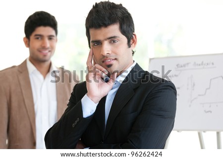 portrait of a happy Indian businessman standing in the boardroom with his colleague in the background