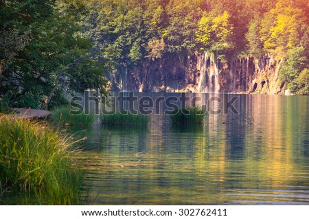 Majestic view on waterfall with turquoise water and sunny beams in the Plitvice Lakes National Park. Forest glowing by sunlight. Croatia. Europe. Retro style.