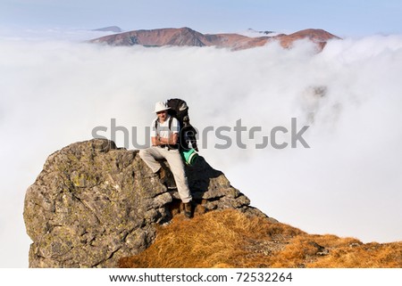 A man with a backpack sitting on the edge of a cliff in the mountains