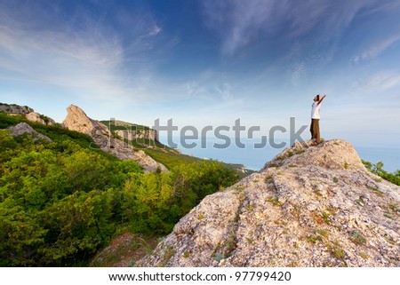 hiker at the top of a rock with his hands up enjoy sunny day