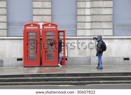 Person photographing a companion posing in a London phone booth