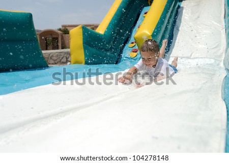 Splashdown! Young boy sliding down an inflatable water slide feet first while splashing water.
