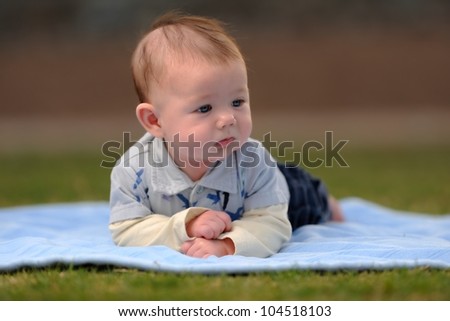 Baby Boy Laying on Front Outside on Blanket. Infant boy laying on a blanket outside while looking to the side. Shallow DOF.