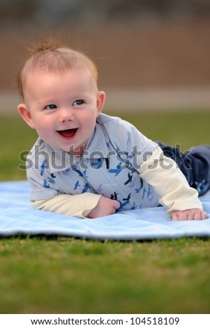 Happy Baby Boy Outside on Blanket. Smiling three-month old baby boy laying on a blue blanket outside. Shallow DOF.