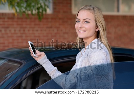 Getting Ready to Drive. Young woman getting in to a car while holding a smartphone.