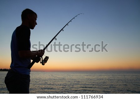 Fisherman fishes on the lake. Silhouette at sunset