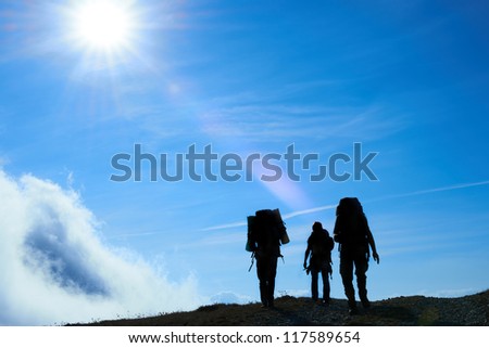 Silhouette of hiking friends against sun and blue sky