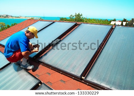Worker mounting solar water heating panels on the roof Worker mounting solar water heating panels on the roof