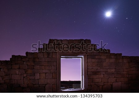 Ruins of ancient city under blue night sky with moon and stars