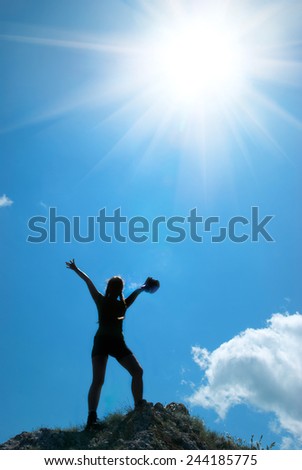Woman on the top of a mountain. Conceptual landscape with blue sky and bright sun background