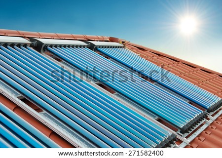 Vacuum collectors- solar water heating system on red roof of the house under shining sun and blue sky