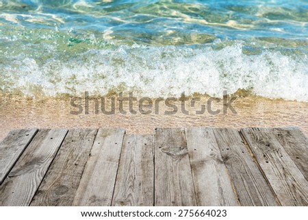 View from empty wooden deck table to tropical sunny beach with surf and blue water background