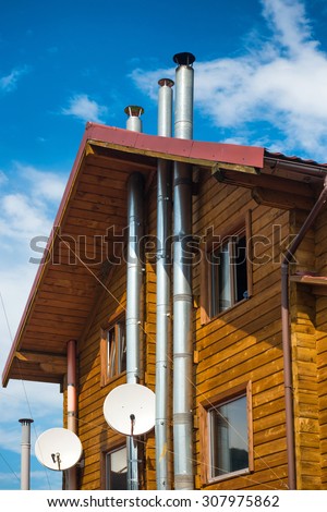 Rural wooden house with modern chimney and satellite tv antenna. Blue sky and clouds on background