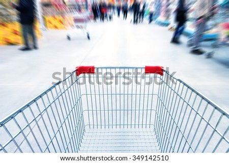 Empty trolley in supermarket or mall full of crowded people. Blur motion.