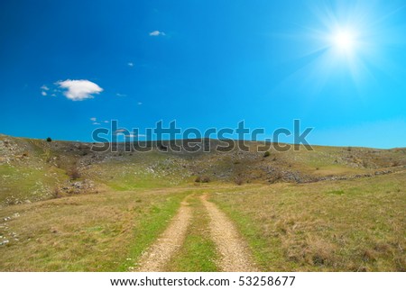 Road over hills with cloudscape and shine sun.