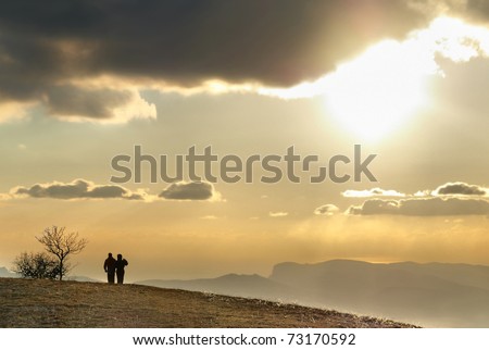 Couple on the hill against sunset. Landscape with clouds and sky.