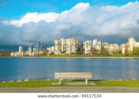 Bench in the green park near sea front with skyscrapers on the background. Vancouver, Canada.