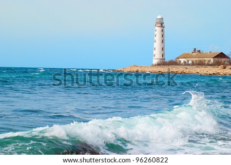 Old lighthouse on the sea coast. Storm, waves and blue sky.