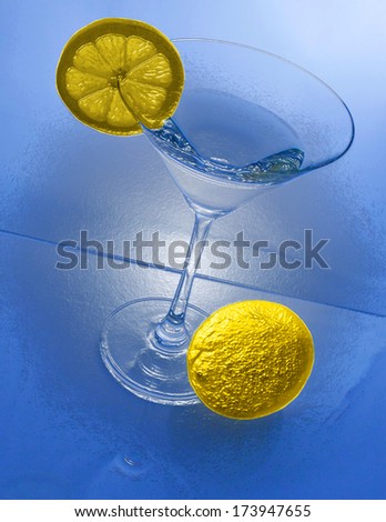 A cocktail glass with a lemon slice and a lemon in front from above view and blue background