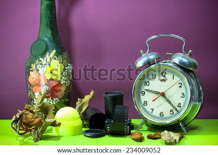 Still life with old broken alarm clock, old glass vase, dead rose, negative film, green golf, colorful background