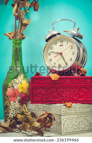 Still life with broken alarm clock, old glass vase with dead rose, vintage boxes, tone image.