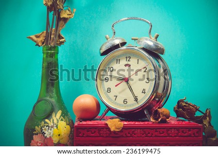 Still life with broken alarm clock, old glass vase with dead rose, egg, vintage box