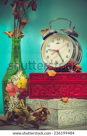 Still life with broken alarm clock, old glass vase with dead rose, vintage boxes, tone image.