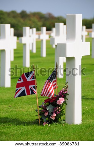 British and American flags and flowery wreath by grave cross in the American war cemetery and memorial in Cambridge, England UK