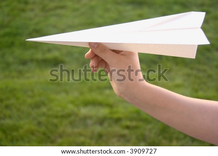 Hand holding a paper airplane with grassy background