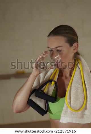 woman in sports clothing drinking water after workout while standing in a training room