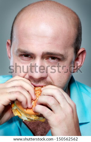 Funny man eating hamburger on grey background