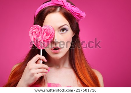 Portrait of beautiful  merry redheaded girl with a large candy on a pink background