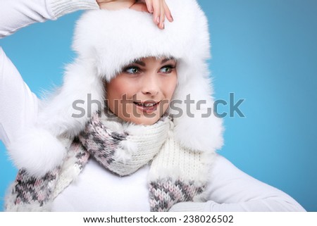 Beautiful merry sexual girl in a white fur cap and warm clothes on a blue background