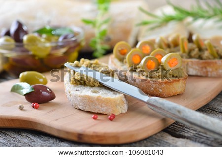 Olive paste on baked olive baguette, decorated with stuffed green olives (stuffed with red bell peppers)